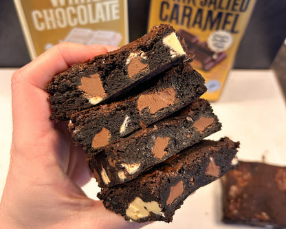 Stack of chocolate brownies held by a hand with Whittaker's chocolate boxes in the background.