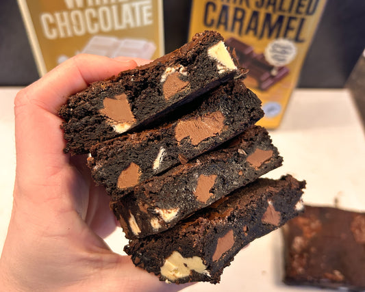 Stack of chocolate brownies held by a hand with Whittaker's chocolate boxes in the background.